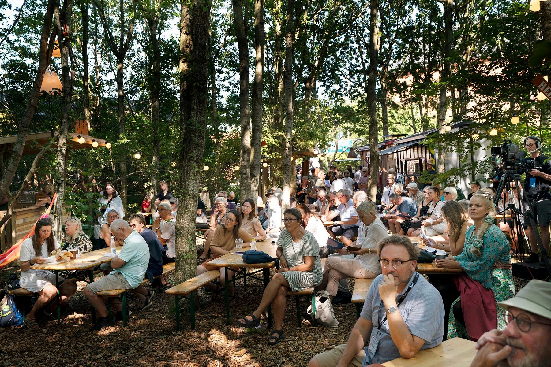 En masse mennesker ved borde og bænke i en skov.